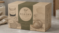 The Baker's Kitchen Complete Sourdough Kit in a kraft paper box with a dark green central band, set on a stone countertop with baking ingredients and utensils in the background.